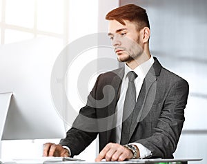 Businessman working with computer in sunny office. Headshot of male entrepreneur at workplace. Business concept