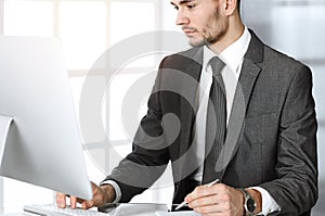 Businessman working with computer in sunny office. Headshot of male entrepreneur at workplace. Business concept