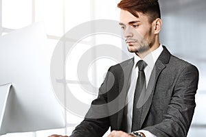 Businessman working with computer in sunny office. Headshot of male entrepreneur at workplace. Business concept