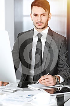 Businessman working with computer in sunny office. Headshot of male entrepreneur at workplace. Business concept