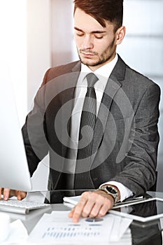 Businessman working with computer in sunny office. Headshot of male entrepreneur at workplace. Business concept