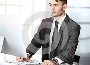 Businessman working with computer in sunny office. Headshot of male entrepreneur at workplace. Business concept