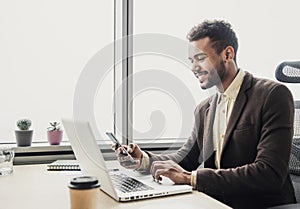 Businessman working on computer. Young smiling man using laptop in the office. Internet marketing, finance, business concept