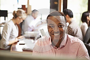 Businessman Working At Desk With Meeting In Background