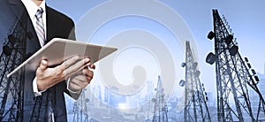 Businessman working digital tablet, with double exposure panoramic cityscape and telecommunication towers in sunrise
