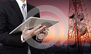 Businessman working on digital tablet, with satellite dish telecom network on telecommunication tower at countryside city in