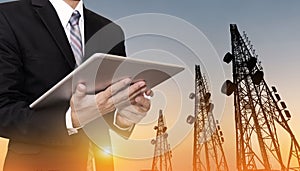 Businessman working on digital tablet, with satellite dish telecom network on telecommunication tower in sunset, telecommunication