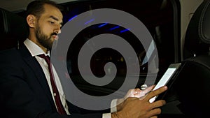 Businessman working on his laptop on the backseat of his luxury car with personal driver
