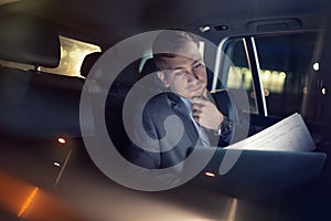Businessman working on his laptop and paper on the back seat of the car