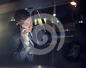 Businessman working on his laptop talking on the phone on the back seat of the car