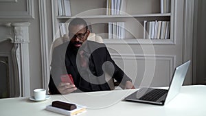 Businessman is working at home, sitting in working room, reading mails in smartphone