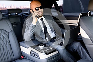 Businessman working on laptop in back seat of Executive car. Concept of business, success, traveling, luxury.