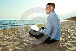 Happy businessman working with laptop on beach. Business trip