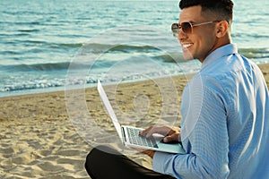 Happy businessman working with laptop on beach. Business trip