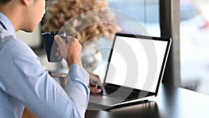 A businessman working on laptop computer and drinking coffee while sitting at workspaceà¹ƒ