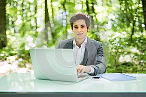 Businessman working on laptop computer in the forest at office table and smile at camera. Business concept.