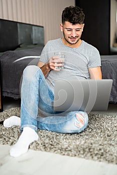 Businessman working on laptop computer sitting at home while drinking water from glass. Man working on laptop computer sitting on