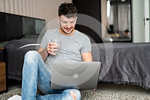 Businessman working on laptop computer sitting at home while drinking water from glass. Man working on laptop computer sitting on