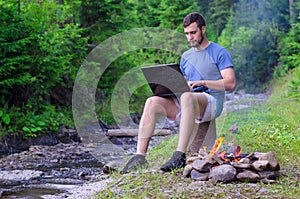 Businessman working on a laptop in a forest near a mountain rive