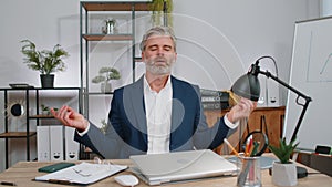 Businessman working on laptop, meditating, doing yoga breathing exercise in lotus position at office