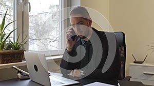 Businessman working on laptop in office making phone call