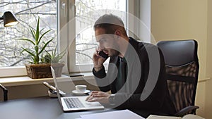 Businessman working on laptop in office making phone call nervous and angry