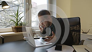 Businessman working on laptop in office making phone call nervous and angry