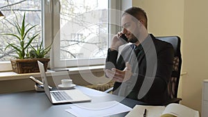 Businessman working on laptop in office making phone call nervous and angry