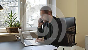 Businessman working on laptop in office taking notes making phone call satisfied with results