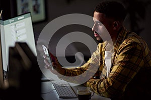 Businessman Working Late In Office With Face Illuminated By Computer Screen Using Mobile Phone