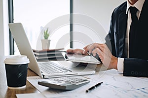 Businessman working new project on laptop computer with report document and analyze, calculating financial data on graph documents