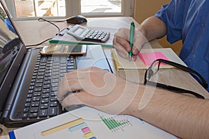 Man working on office desk with Calculator, a computer, a pen and document. Man counting money and making calculations
