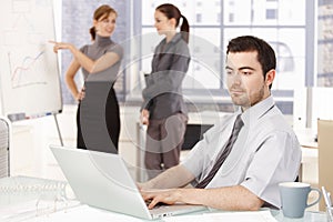 Businessman working in office women in background