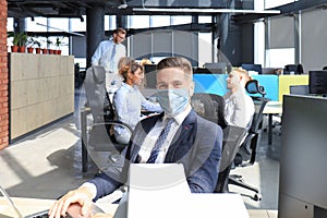 Businessman is working in preventive medical mask in the epidemic in office, collegues at the background