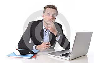 Businessman working in stress at office desk computer laptop reflexive and doubtful pensive and thoughtful