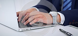 Businessman working by typing on laptop computer. Man`s hands on notebook or business person at workplace. Employment o