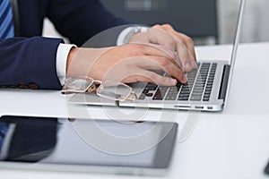 Businessman working by typing on laptop computer. Man`s hands on notebook or business person at workplace. Employment o