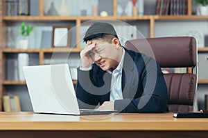 Businessman worried about business, sad and frustrated sitting in the office, looking anxiously at the laptop screen