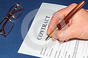 Businessman writes a contract on blue table in the office or bank, hand holds a pen