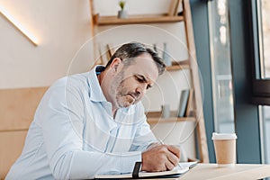 concentrated mature businessman writing in notebook