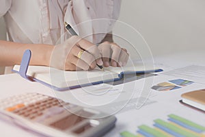 Businessman writing on notebook on wooden table, People are recording accounting data calculated from calculator.