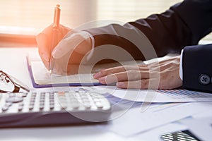 Businessman writing on notebook on wooden table, People are recording accounting data calculated from a calculator.