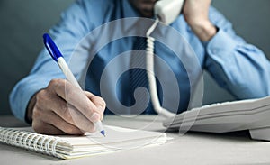 Businessman writing on notepad and talking in office telephone. Contact concept