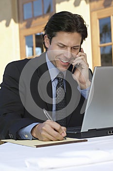 Businessman Writing Notes While On Call