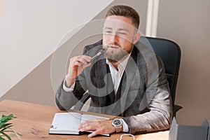 Businessman writing notes while sitting at his desk. Young bearded man