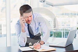 Businessman writing and phoning at his desk