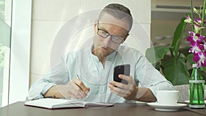 Businessman writing in daily planner and check notes on smartphone