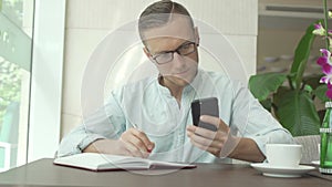 Businessman writing in daily planner and check notes on smartphone