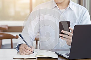 Businessman writing something idea on note or check list and using smartphone with computer laptop, Working and Planning concept
