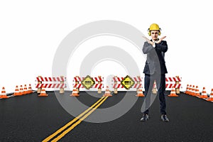 Businessman in yellow helmet and headphones standing on the road under construction with his arms crossed in stop